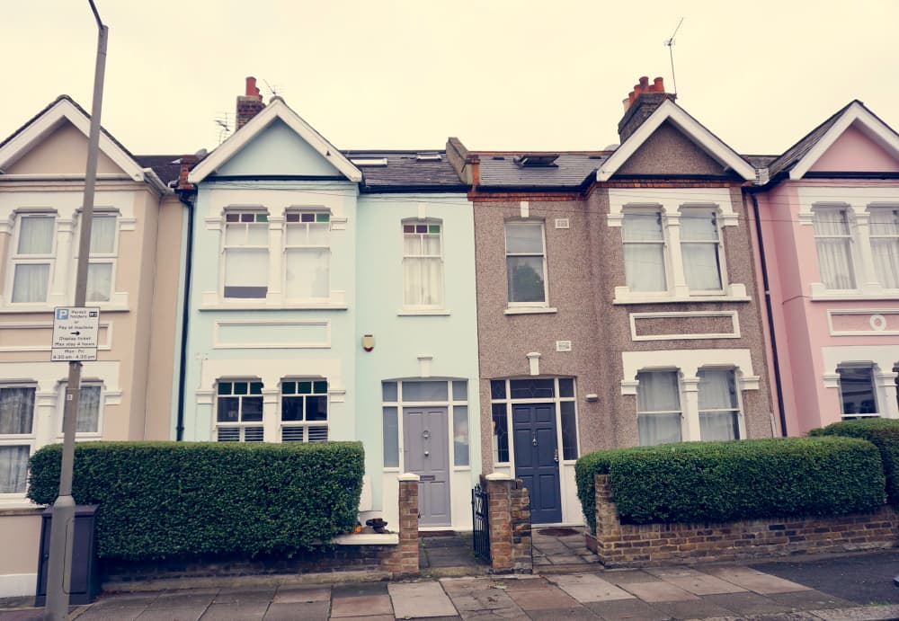 Row of pastel-colored terraced houses on a cloudy day. Houses are in beige, blue, gray, and pink.