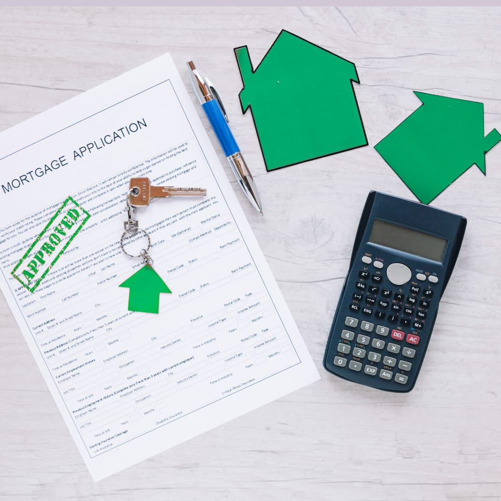 A mortgage application with an "Approved" stamp lies on a table with keys, a pen, a calculator, and greenhouse cutouts.