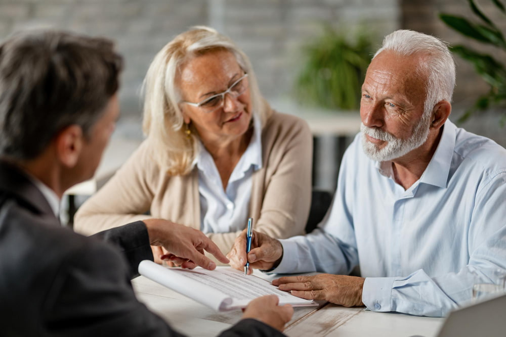 Elderly couple signs documents with a professional—man focused, woman attentive—creating a serious, collaborative mood.